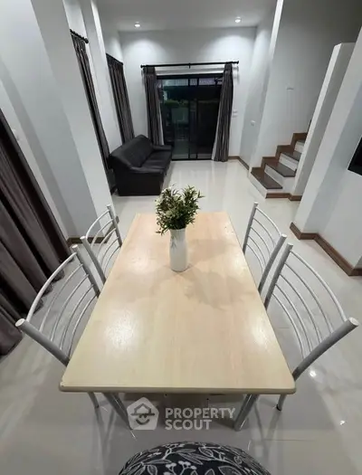 Modern dining area with sleek table and chairs, adjacent to cozy living room and staircase.