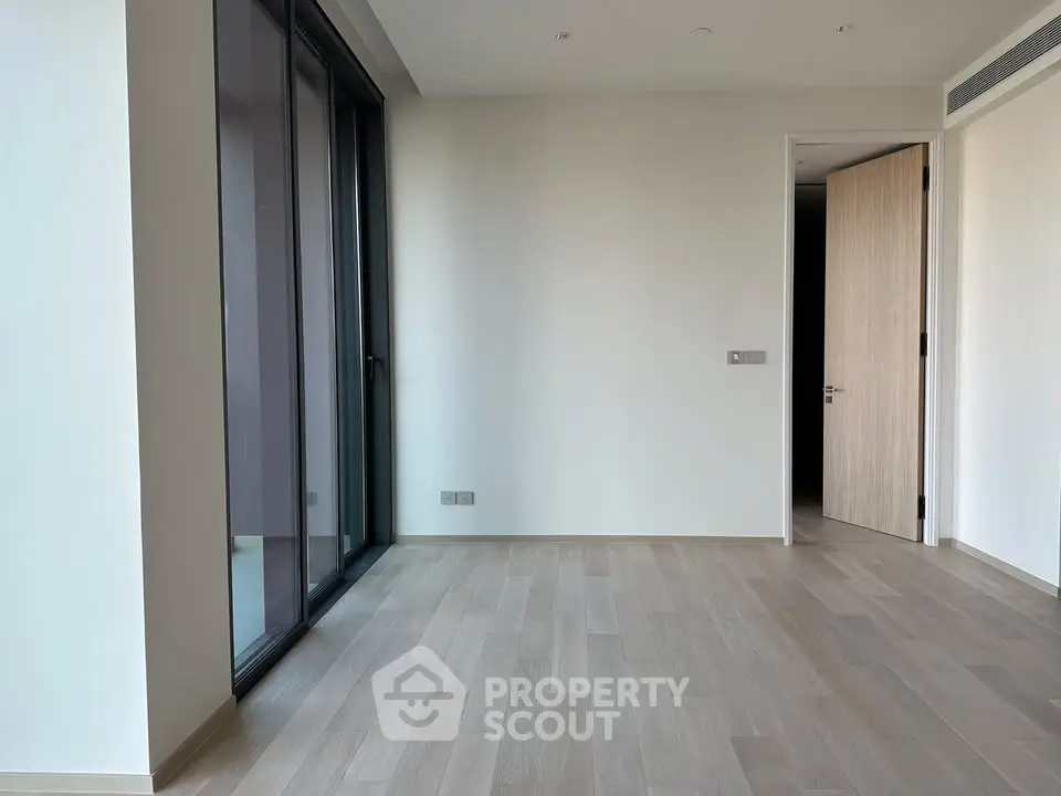 Spacious empty room with large windows and wooden flooring in modern apartment.