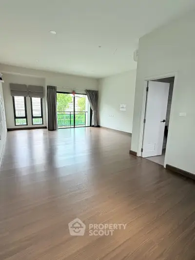 Spacious empty living room with large windows and balcony access, featuring elegant wooden flooring.