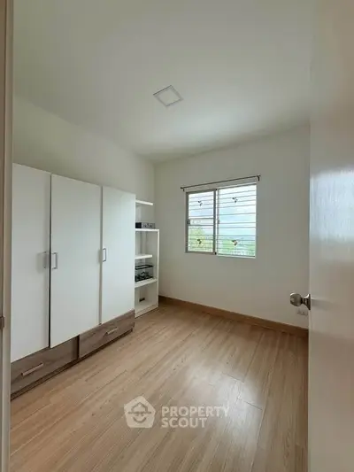 Spacious bedroom with modern wardrobe and natural light through window.