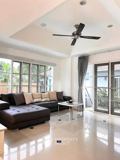 Spacious living room with modern sofa and ceiling fan, large windows offering natural light.