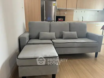 Modern living room with sleek gray sofa and stainless steel fridge in open kitchen layout.
