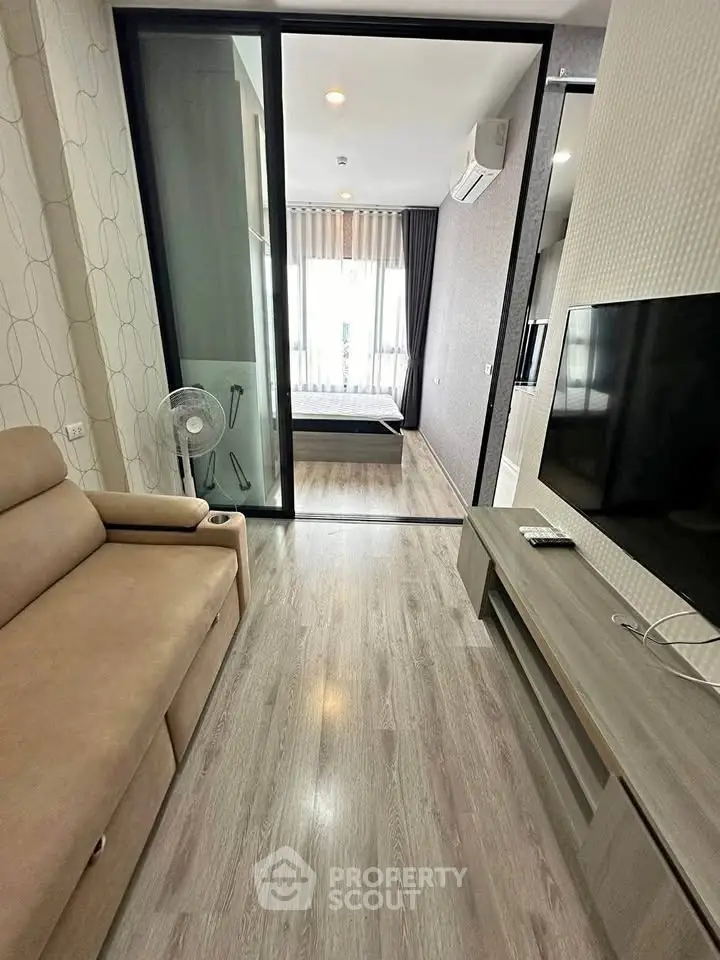 Modern apartment living room with sliding glass door to bedroom, featuring sleek furniture and wood flooring.