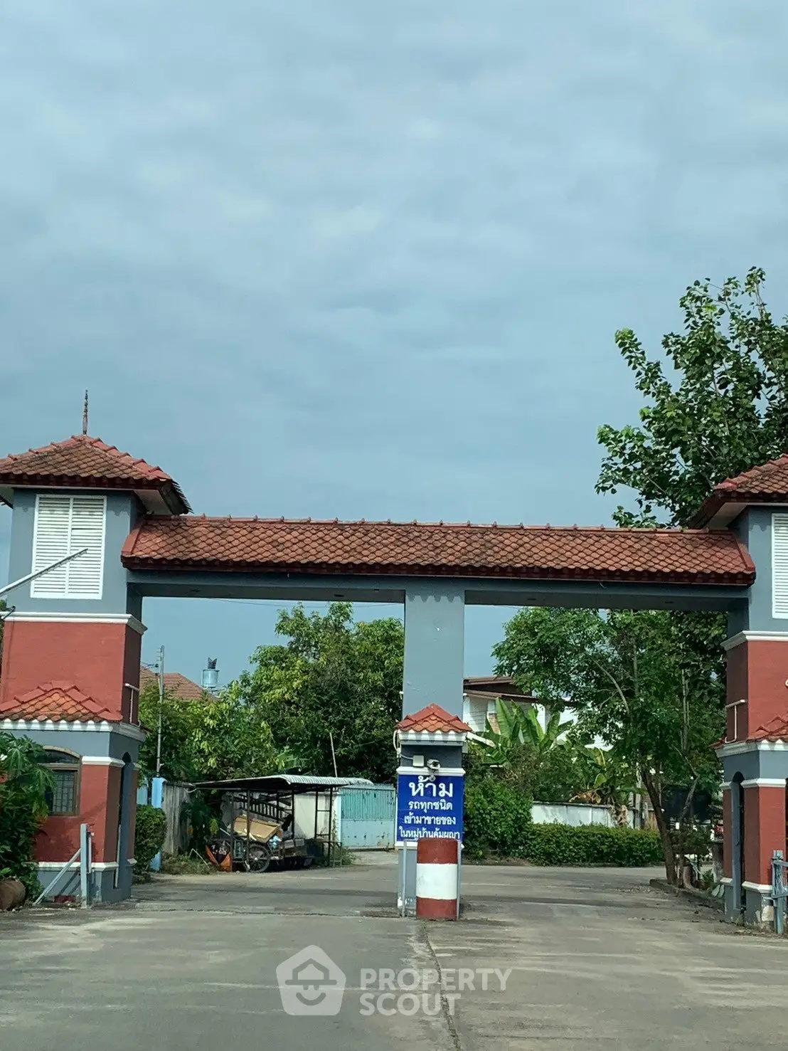 Charming gated entrance of residential community with red-tiled roofs and lush greenery.