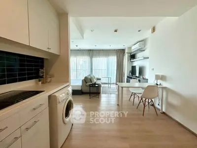 Modern open-plan living room with kitchen and washing machine, featuring sleek furniture and natural light.
