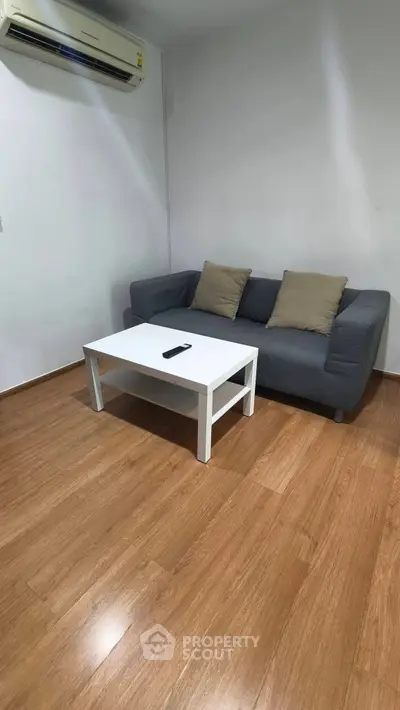 Cozy living room with modern sofa, wooden flooring, and air conditioning for comfort.