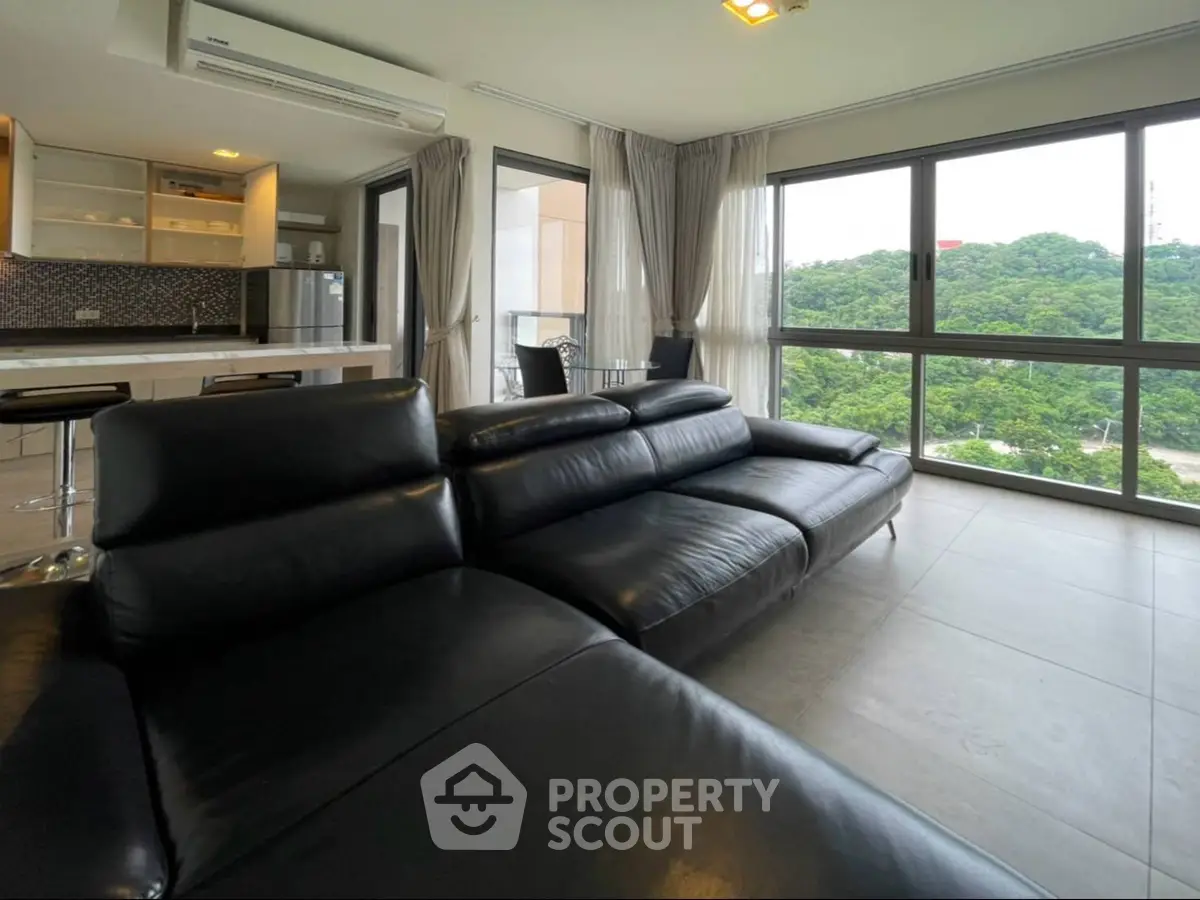Luxurious modern living room with panoramic forest views and sleek black leather sofa.