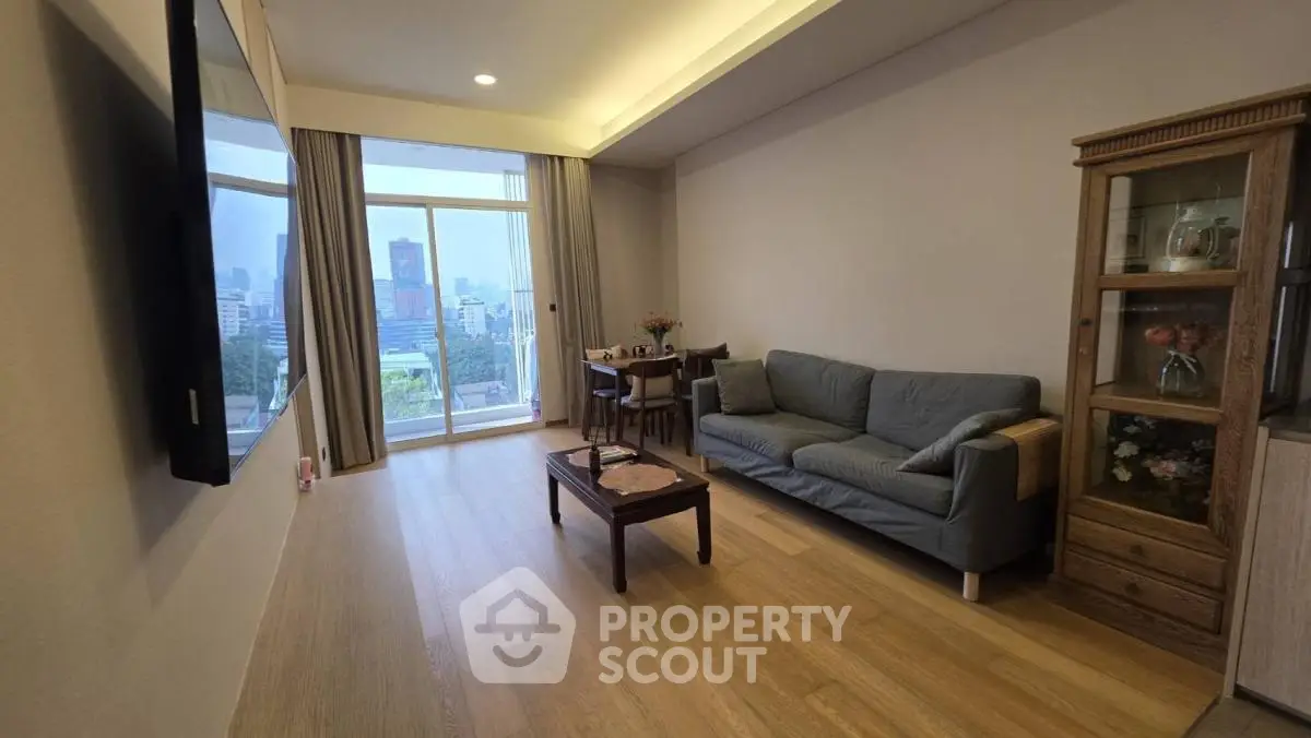 Spacious living room with large window offering stunning city view, cozy seating, and elegant wooden flooring.