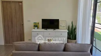 Cozy living room with modern decor and natural light, featuring a TV and stylish furniture.