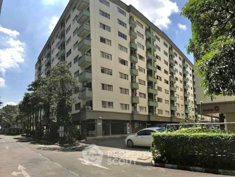 Modern multi-story apartment building with lush greenery and parking area, ideal urban living.