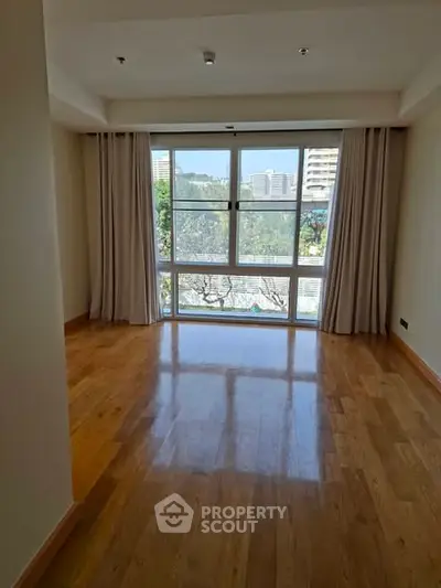 Spacious empty room with large window and wooden flooring, offering a bright and airy atmosphere.