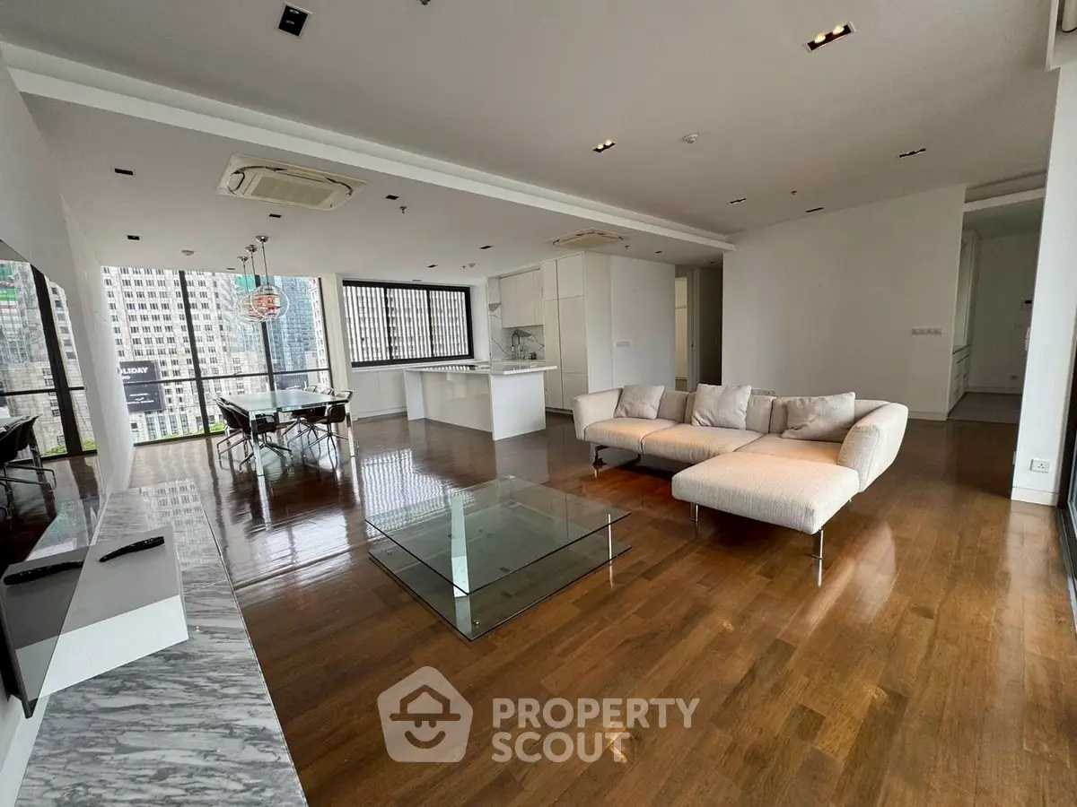 Spacious modern living room with open kitchen and city view, featuring elegant furniture and wooden flooring.