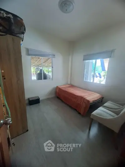 Cozy bedroom with natural light and minimalist decor, featuring a single bed and comfortable seating.