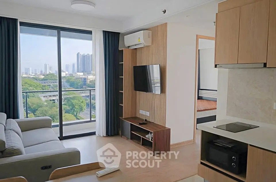 Modern living room with city view, featuring sleek furniture and open kitchen layout.