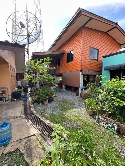 Charming two-story wooden house with lush garden and satellite dish, perfect for serene living.