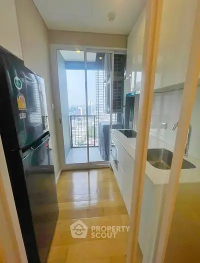 Modern kitchen with balcony view, sleek appliances, and wooden flooring in urban apartment.