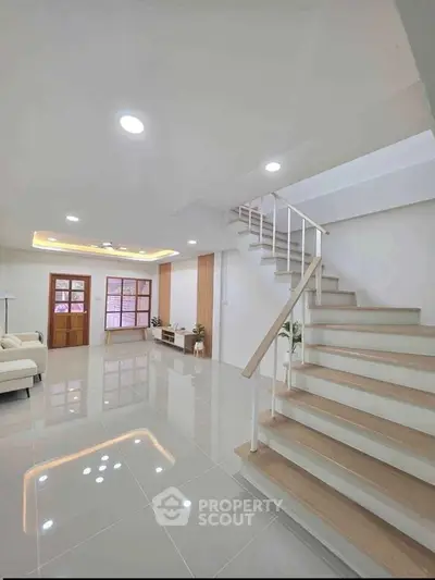Spacious modern living room with elegant staircase and glossy tiled floor.