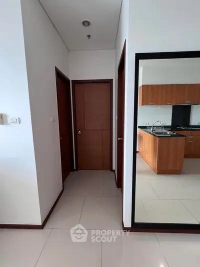 Modern apartment interior with sleek kitchen and hallway, featuring wooden cabinetry and tiled flooring.