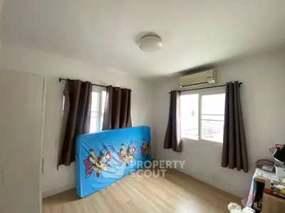 Cozy bedroom with wooden flooring and air conditioning, featuring natural light from two windows.