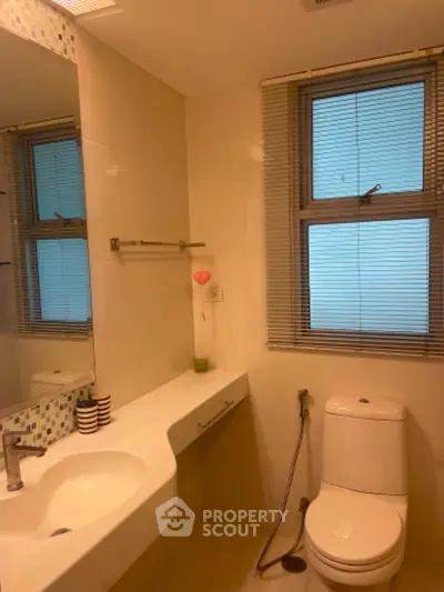 Modern bathroom with sleek design and large mirror, featuring a window with blinds.