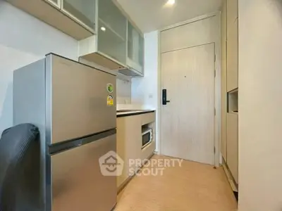 Modern compact kitchen with stainless steel fridge and microwave in cozy apartment.