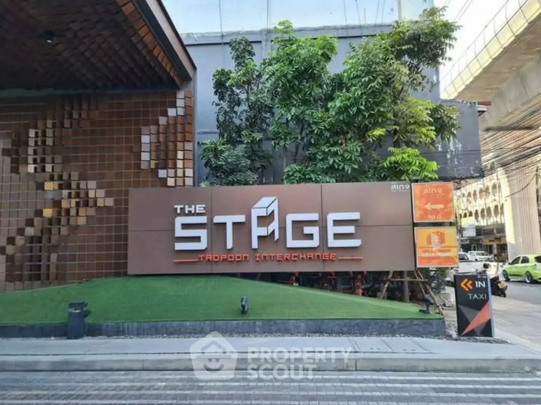 Modern building entrance with stylish signage at The Stage, featuring lush greenery and urban design.