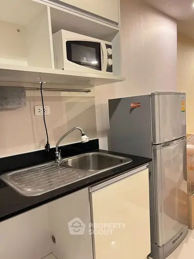 Modern kitchen with sleek cabinetry, stainless steel sink, microwave, and refrigerator in a compact layout.