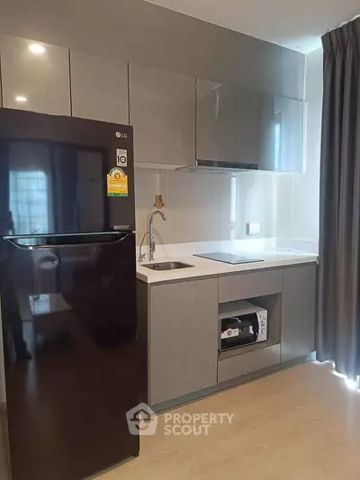 Modern kitchen with sleek cabinetry and black fridge in stylish apartment.