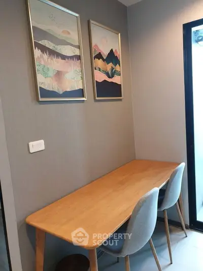 Modern study nook with wooden desk and stylish chairs, featuring artistic wall decor and natural light.