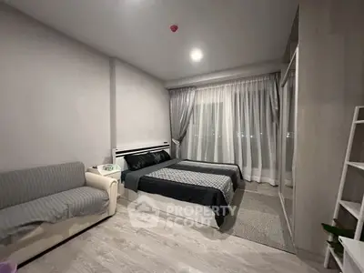 Modern bedroom with cozy bed, stylish sofa, and large window with sheer curtains.