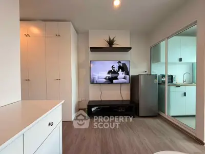 Modern living room with sleek kitchen and built-in storage, featuring a wall-mounted TV and stylish decor.