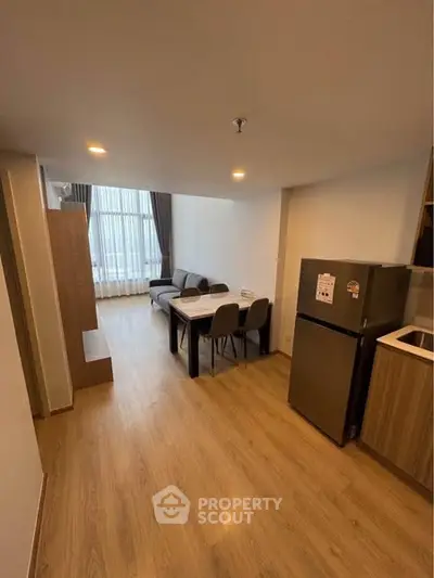 Modern living room with dining area and kitchen, featuring sleek furniture and wooden flooring.