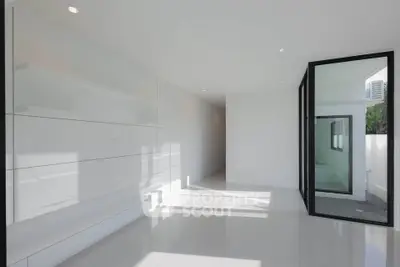 Modern minimalist interior with sleek white walls and large glass door, offering ample natural light.