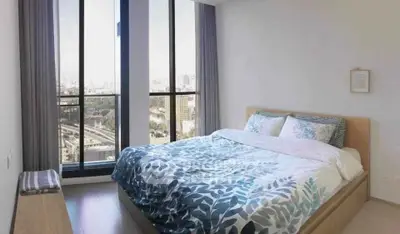 Spacious bedroom with floor-to-ceiling windows offering stunning city views, modern decor, and ample natural light.