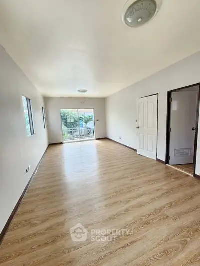 Spacious empty room with wooden flooring and large windows for natural light.