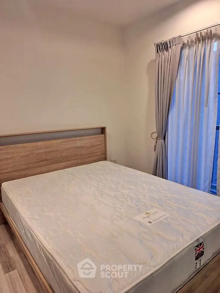 Cozy bedroom with wooden bed frame and large window with curtains, perfect for relaxation.
