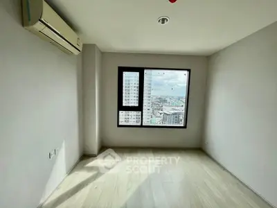 Bright empty room with large window and city view, featuring air conditioning and light wood flooring.