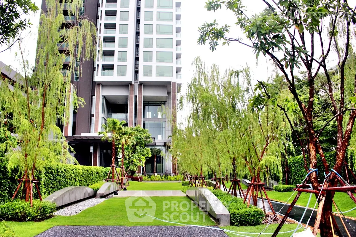 Luxurious modern apartment building with lush landscaped garden and trees.