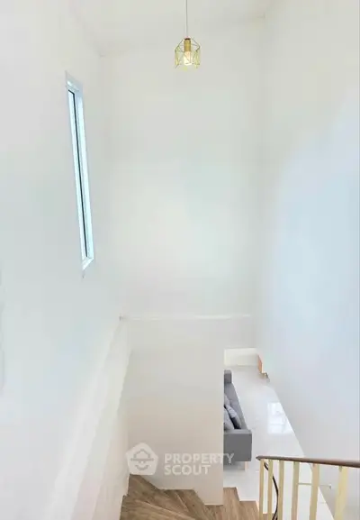 Bright minimalist staircase with modern pendant light and glimpse of cozy living room.