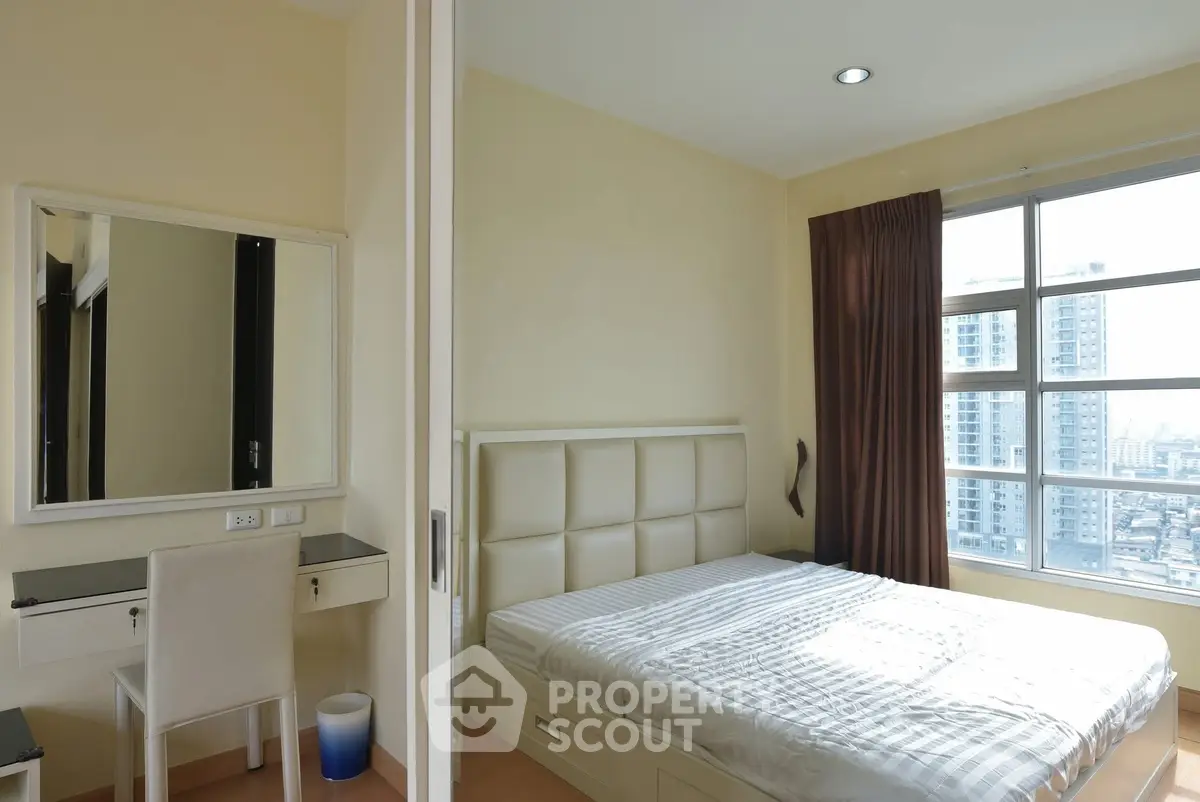 Bright bedroom with large window and city view, featuring a modern bed and vanity desk.