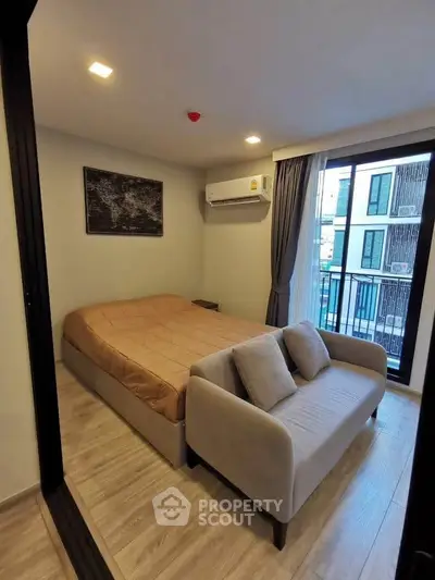 Cozy bedroom with modern decor and small balcony access, featuring a comfortable bed and stylish sofa.