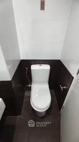 Compact modern bathroom with sleek white toilet and dark tile accents.