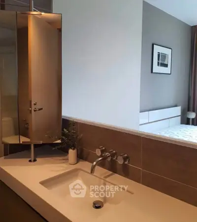 Modern bathroom with sleek sink and mirror, adjacent to a stylish bedroom.