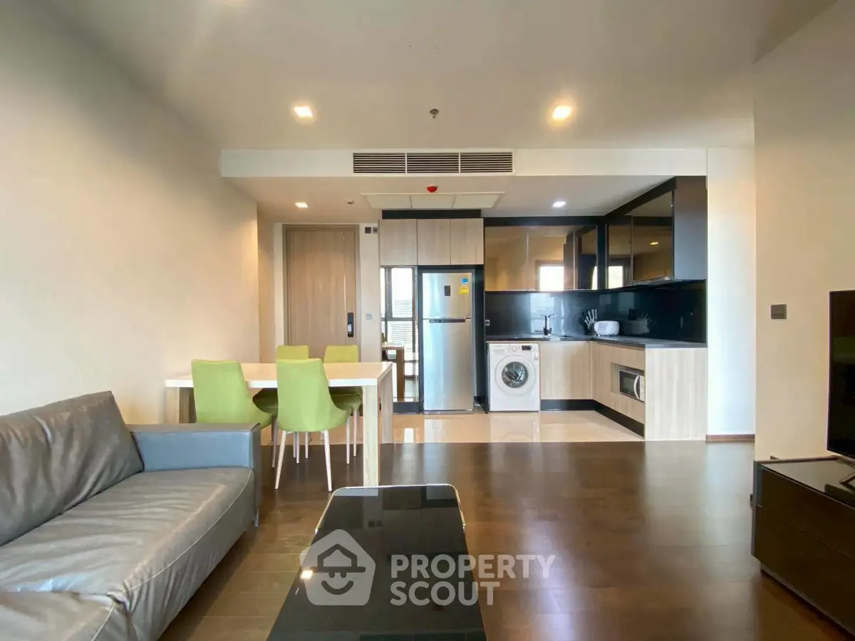Modern open-plan living room with kitchen, featuring sleek furniture and built-in appliances.