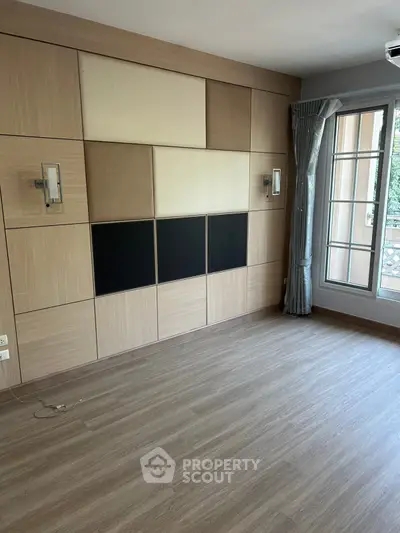 Spacious empty room with modern wood paneling and large window for natural light