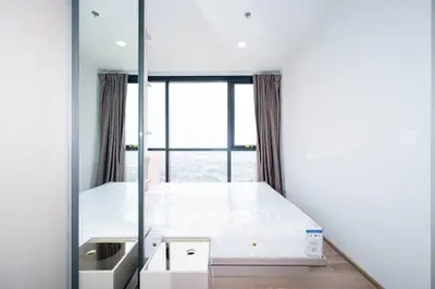 Bright and modern bedroom with large window offering stunning city views, featuring a comfortable bed and sleek design.