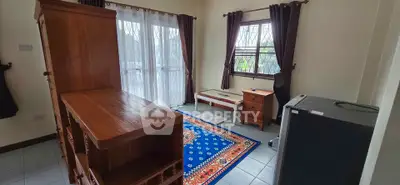 Cozy living room with wooden furniture and vibrant rug, natural light through large windows.