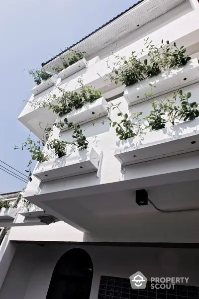 Modern white building facade with lush green balcony plants, showcasing contemporary urban living.