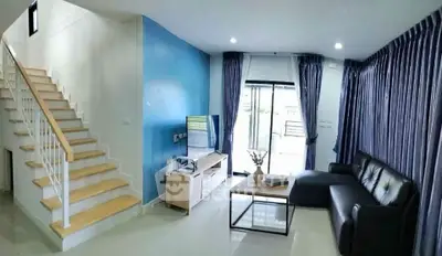 Modern living room with staircase and large windows, featuring sleek furniture and blue accent wall.