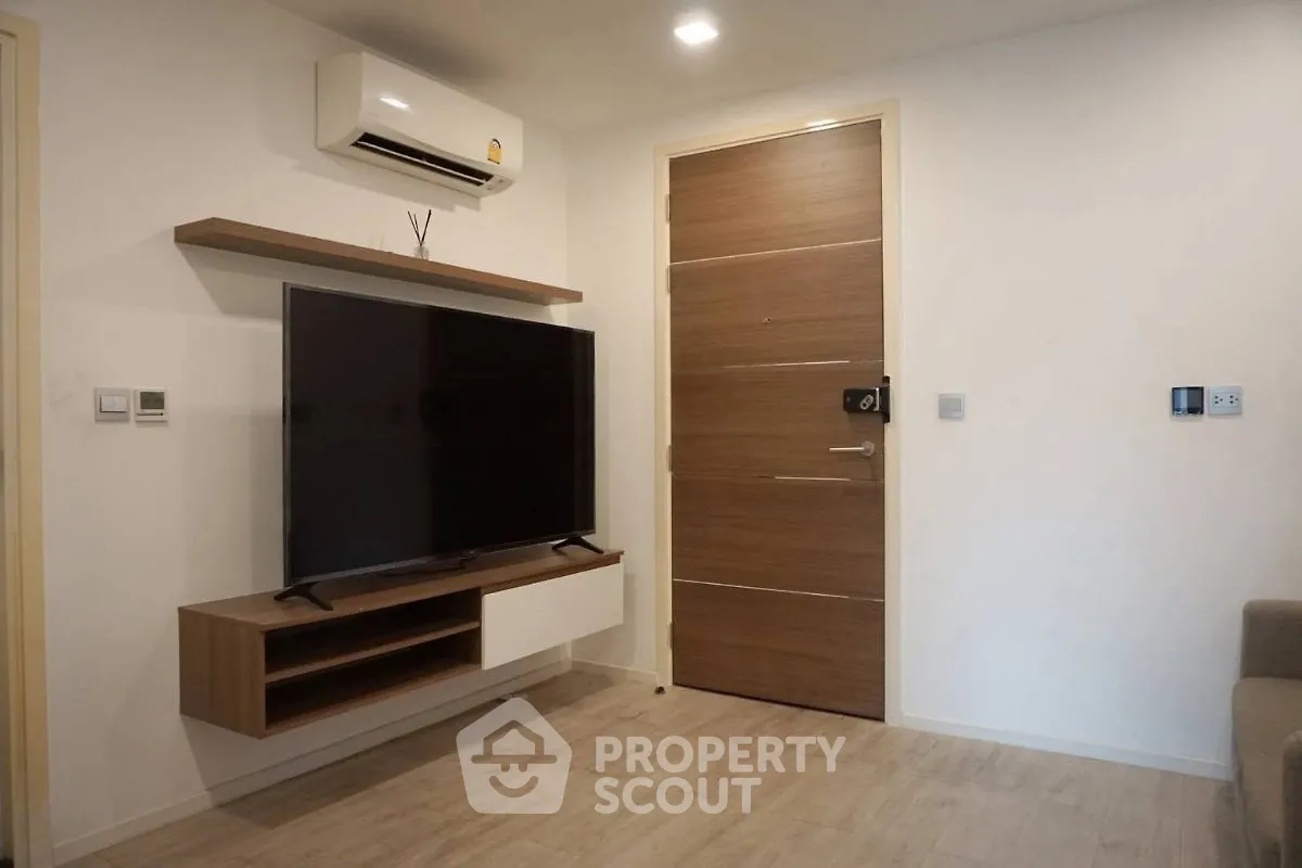 Modern living room with wall-mounted TV and air conditioning unit, featuring sleek wooden flooring and door.